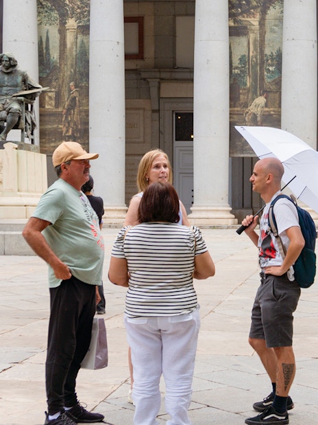 Guide discussing artwork with tourists outside Prado Museum, Madrid.