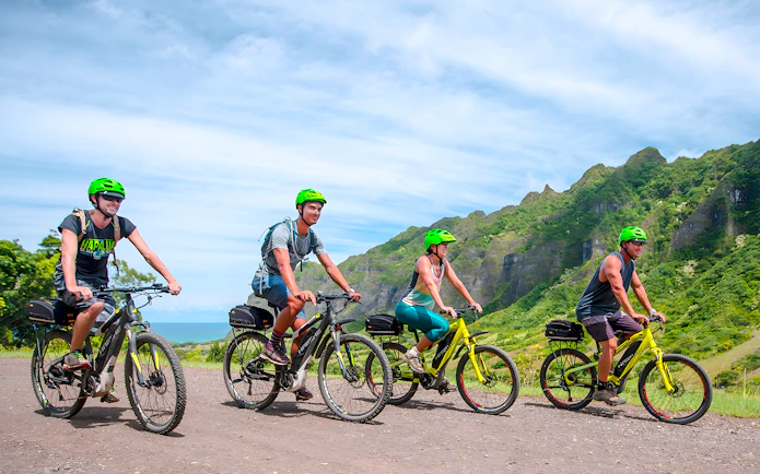 Novice riders on e-bikes touring Kualoa Ranch with lush mountains in the background.