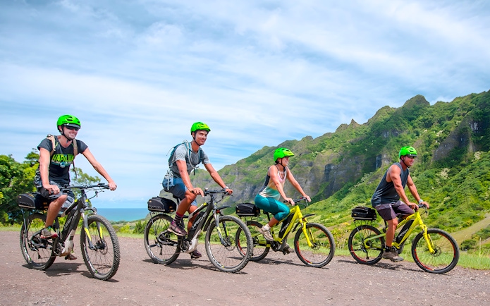 Novice riders on e-bikes touring Kualoa Ranch with lush mountains in the background.