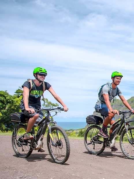Novice riders on e-bikes touring Kualoa Ranch with lush mountains in the background.