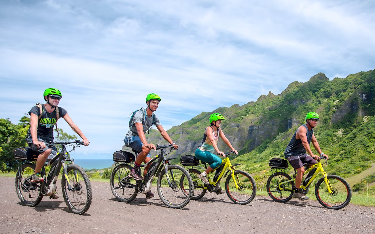 Novice riders on e-bikes touring Kualoa Ranch with lush mountains in the background.
