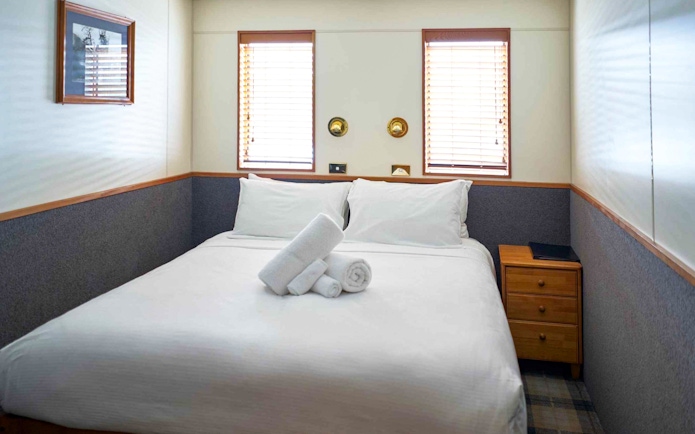Cozy cabin bedroom with double bed and towels on an Overnight Milford Sound Cruise.