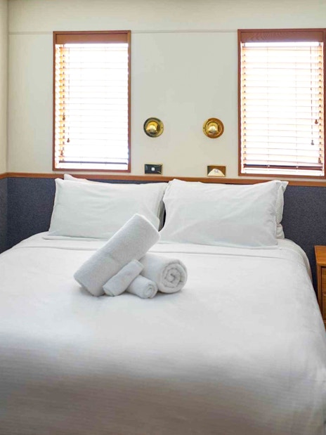 Cozy cabin bedroom with double bed and towels on an Overnight Milford Sound Cruise.