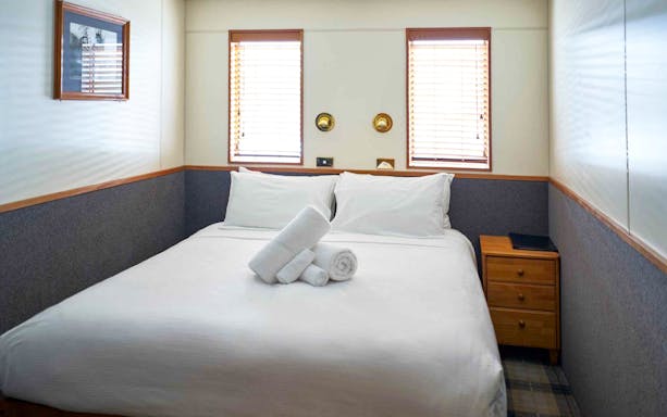 Cozy cabin bedroom with double bed and towels on an Overnight Milford Sound Cruise.