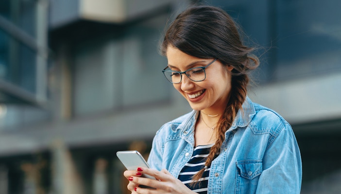 Woman smiling while reading a message on her phone outdoors.