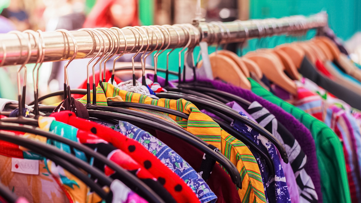 Street shop displaying vintage clothing in a bustling market setting.