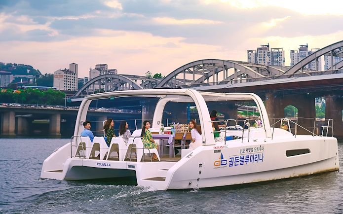 Yacht on Han River with people enjoying a scenic cruise near a bridge in Seoul.