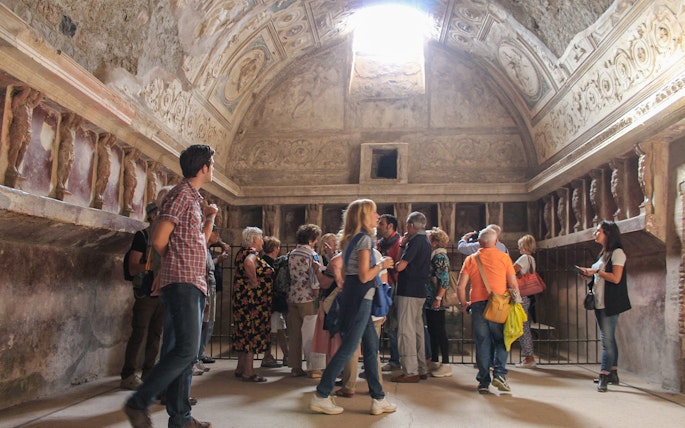 Tourists with a guide exploring an ancient room in the ruins of Pompeii, Italy.