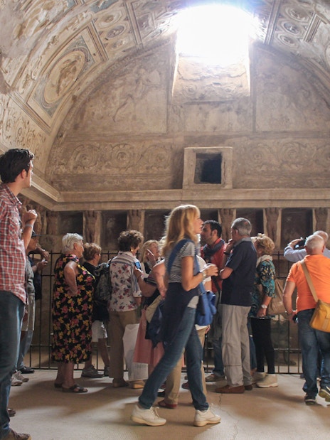 Tourists with a guide exploring an ancient room in the ruins of Pompeii, Italy.