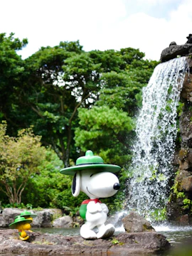 Snoopy statue by a waterfall in Snoopy Garden, surrounded by lush greenery.