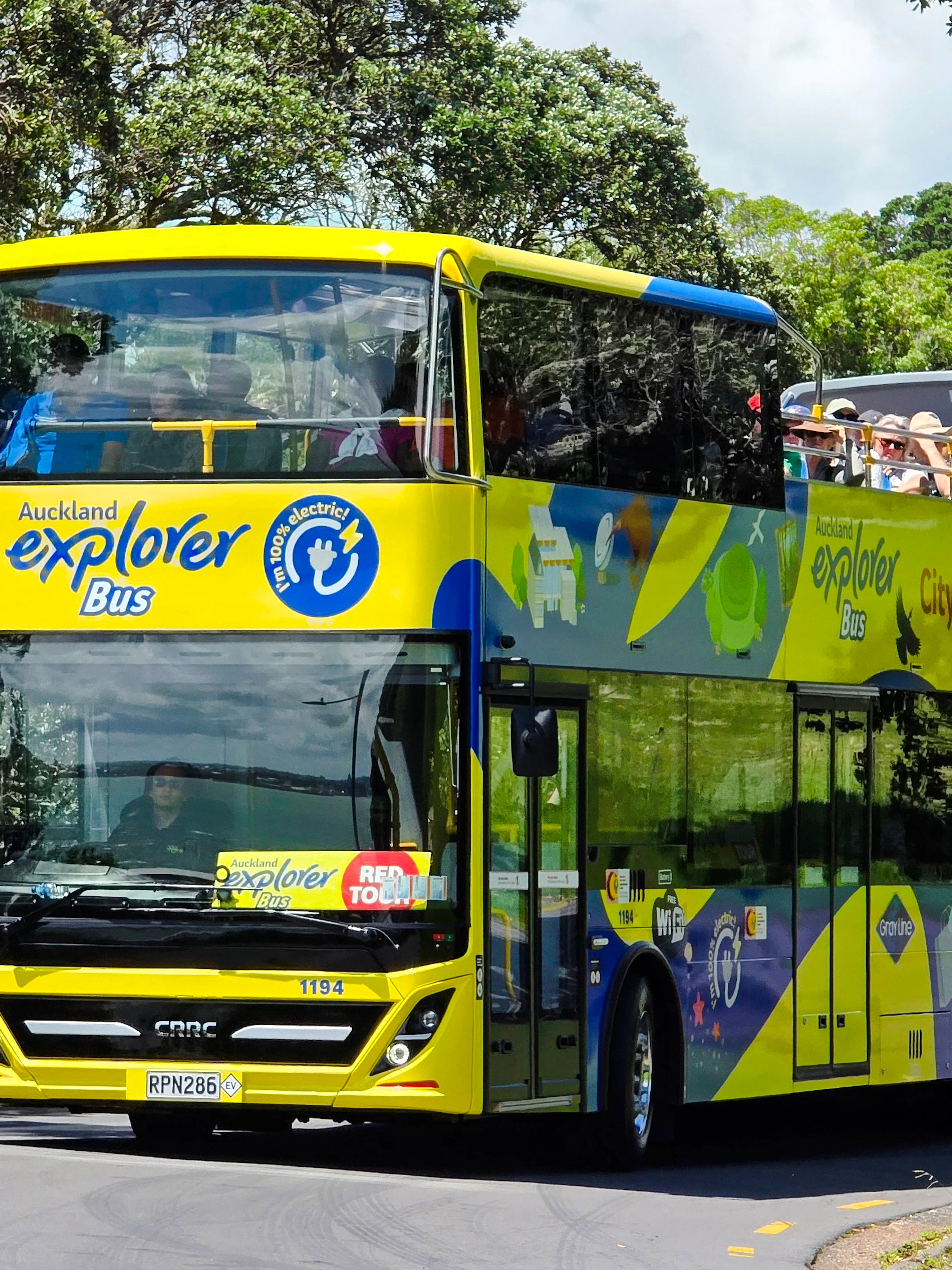 Auckland Explorer Bus on a sunny day with tourists on the upper deck.