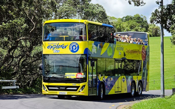 Auckland Explorer Bus on a sunny day with tourists on the upper deck.