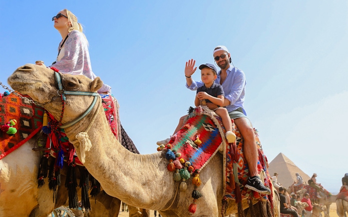 Tourists riding camels near the Giza Pyramids and Sphinx in Egypt.