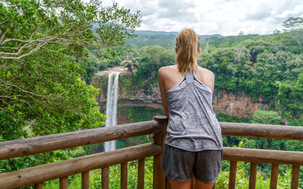 Person viewing Chamarel Waterfall from a wooden lookout, Mauritius.