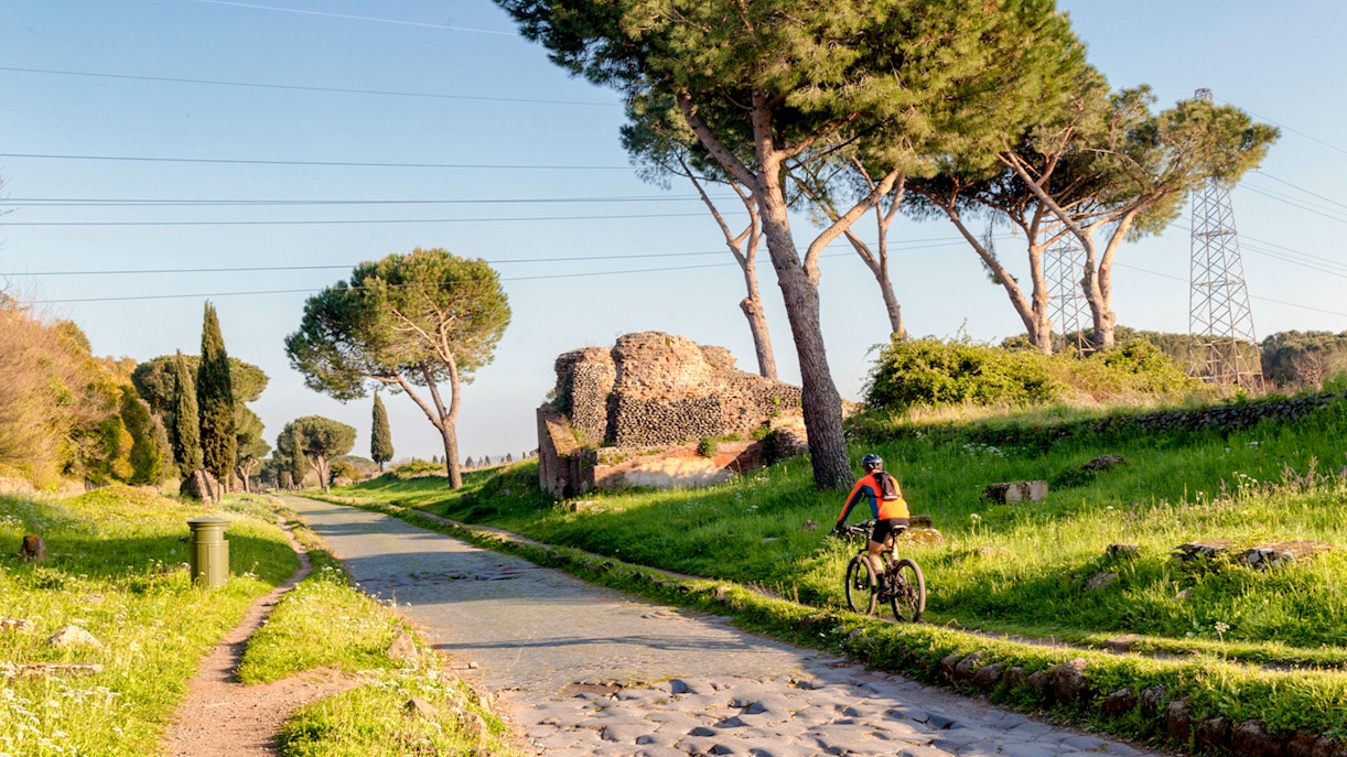 Via Appia Antica in Rome with mausoleum, pine trees, and a bicycle on the path.