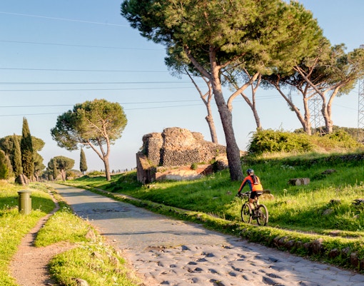Via Appia Antica in Rome with mausoleum, pine trees, and a bicycle on the path.