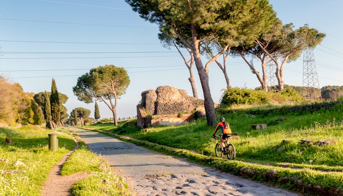 Via Appia Antica in Rome with mausoleum, pine trees, and a bicycle on the path.