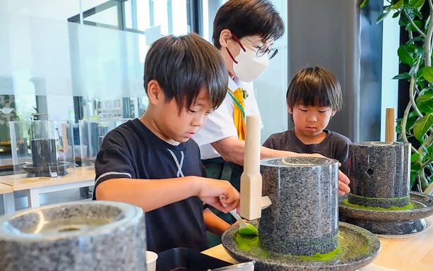 Kids learning to make matcha with traditional tools in a class.