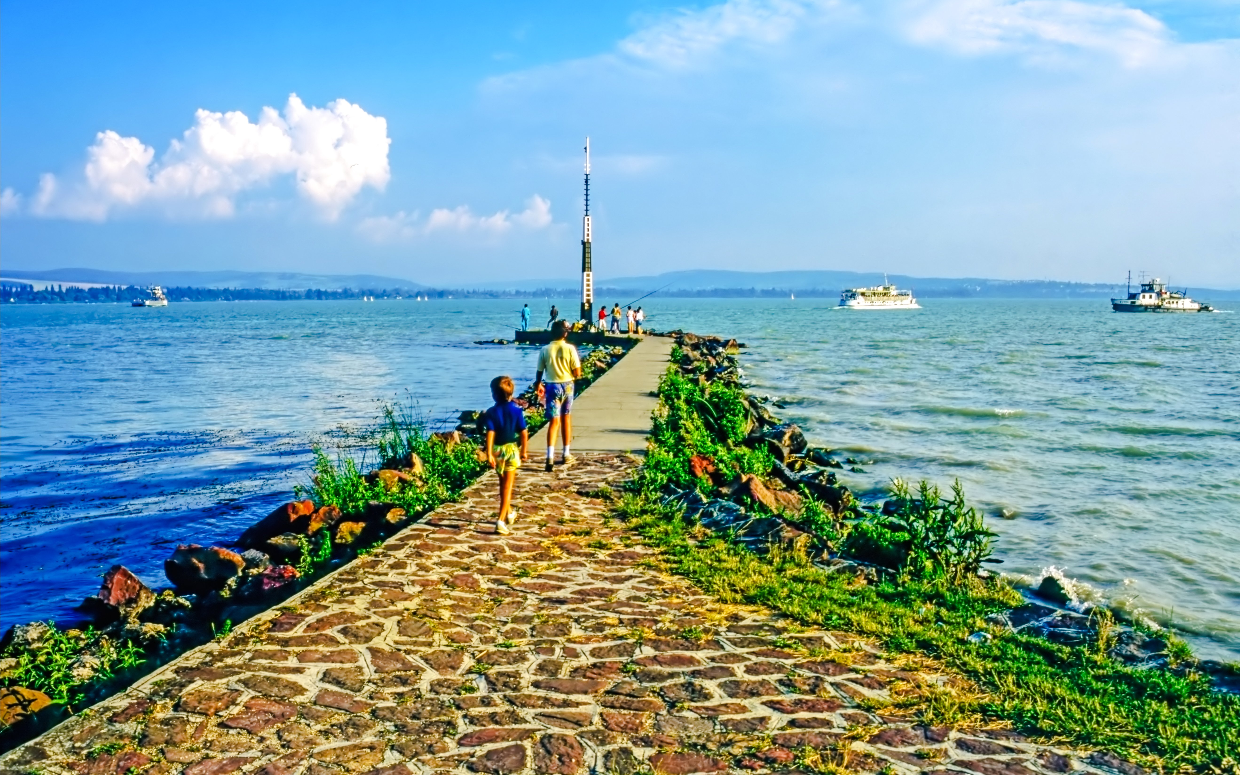 Visitors walking on a pier at Lake Balaton, Hungary, with boats in the distance.