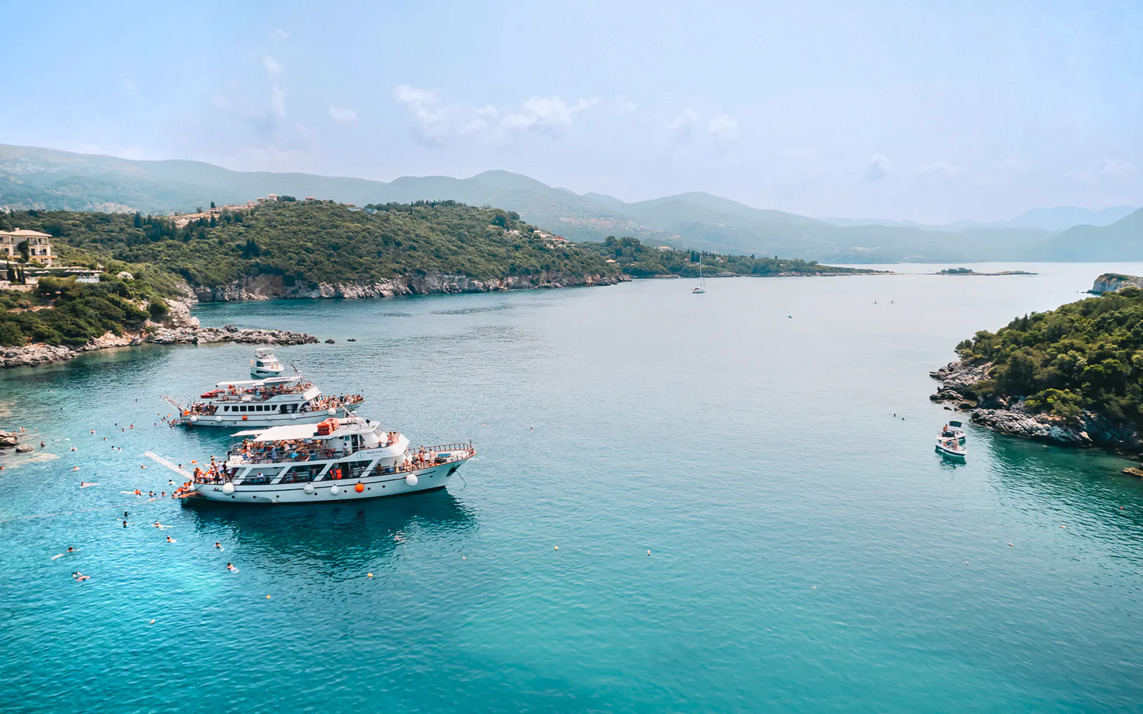 Cruise boats in Blue Lagoon, Greece, with swimmers in clear water near Benitses/Lefkimmi.