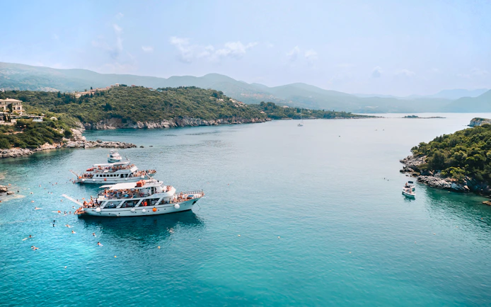 Cruise boats in Blue Lagoon, Greece, with swimmers in clear water near Benitses/Lefkimmi.