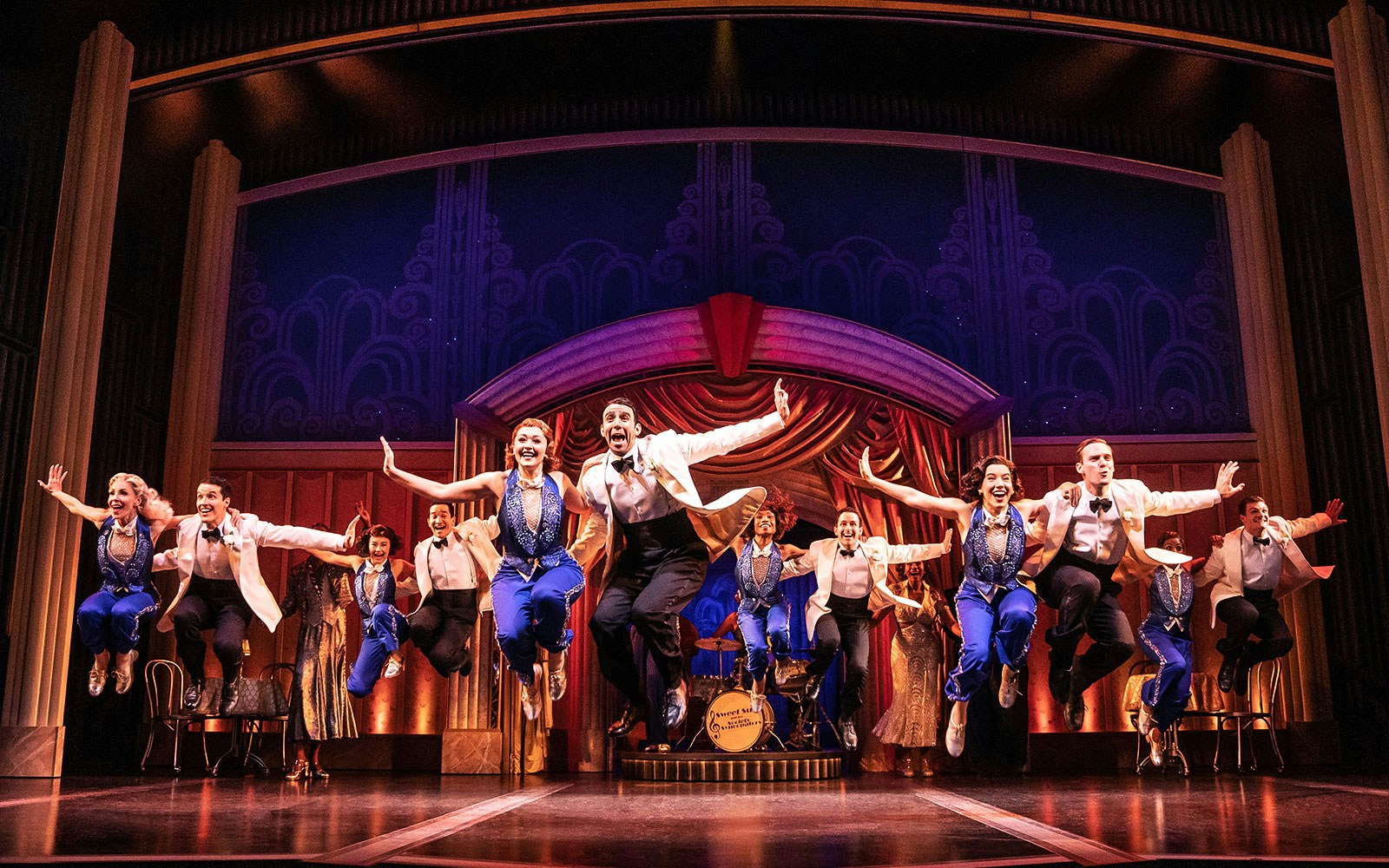Performers in mid-air during a musical number from "Some Like it Hot" on stage.