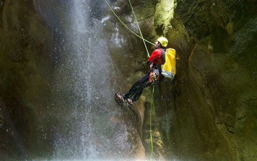Canyoneer rappelling down a waterfall during Chli Schliere canyoning experience near Interlaken.