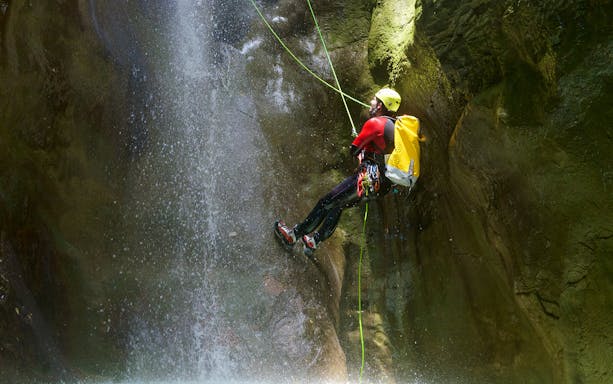 Canyoneer rappelling down a waterfall during Chli Schliere canyoning experience near Interlaken.