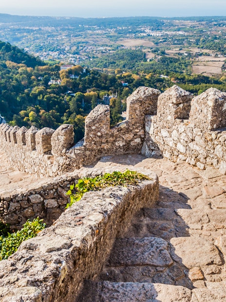 Stone pathway along the walls of Moorish Castle, Sintra, with scenic valley view.