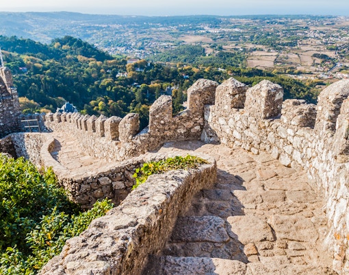 Stone pathway along the walls of Moorish Castle, Sintra, with scenic valley view.