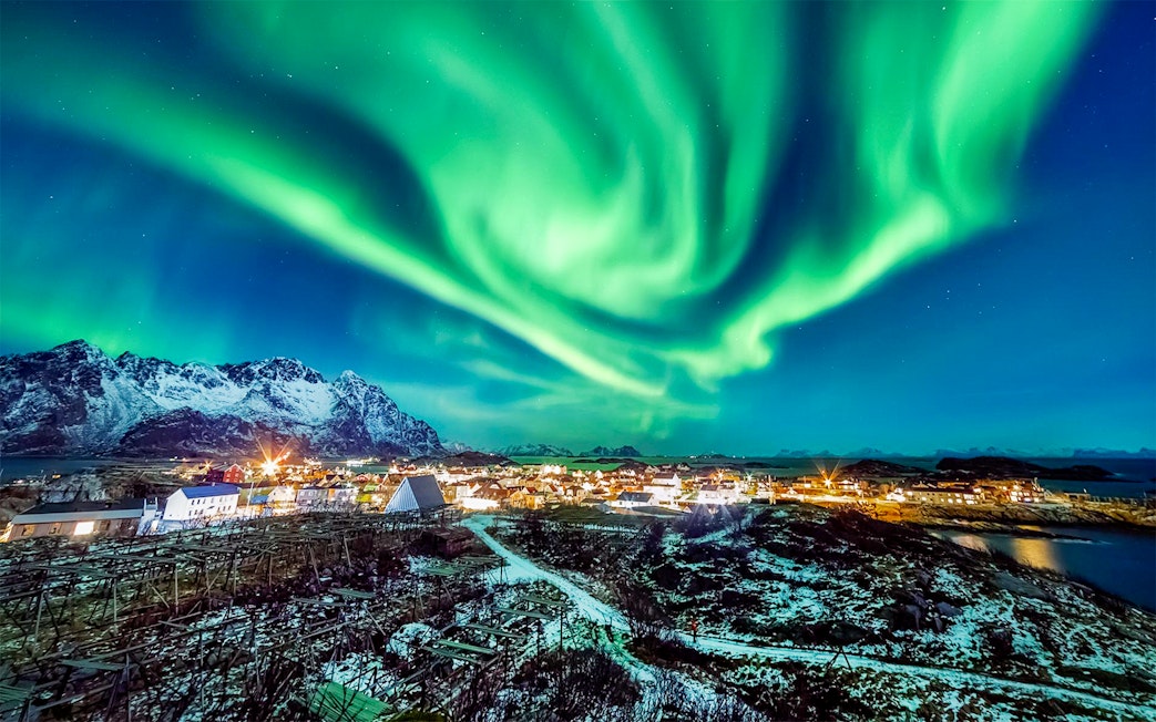 Northern Lights over snowy village and mountains in Norway.