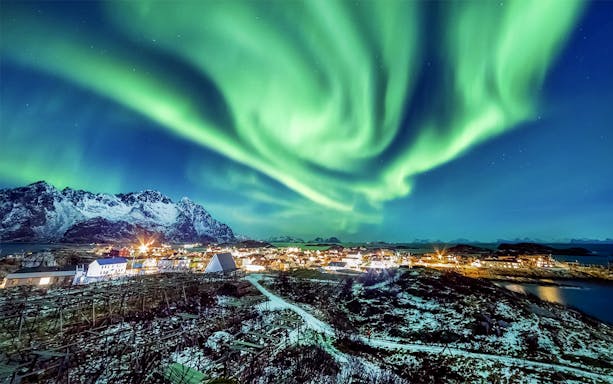 Northern Lights over snowy village and mountains in Norway.