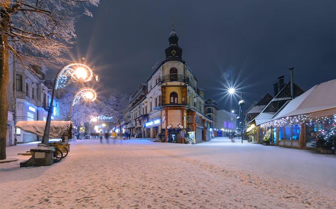 Snow-covered street in Zakopane at night with festive lights and historic buildings.
