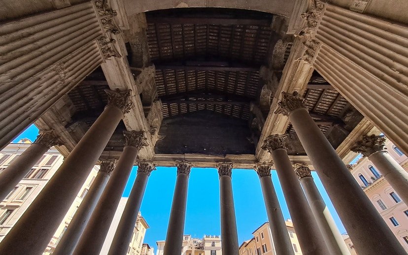 Columns of the Pantheon in Rome viewed from below against a clear blue sky.