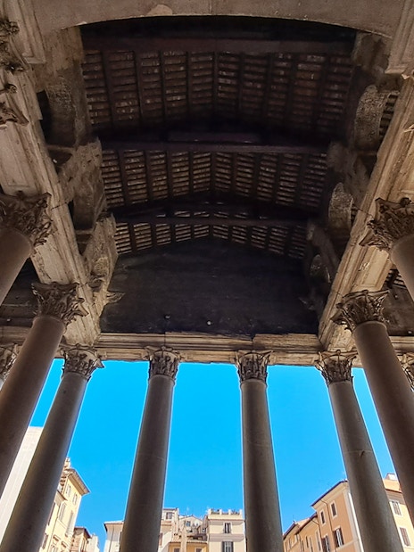 Columns of the Pantheon in Rome viewed from below against a clear blue sky.