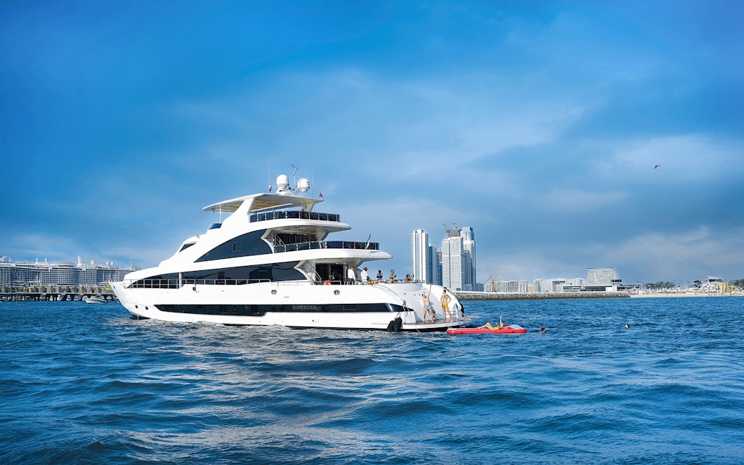 Superyacht TriDeck cruising near city skyline with people enjoying water activities.