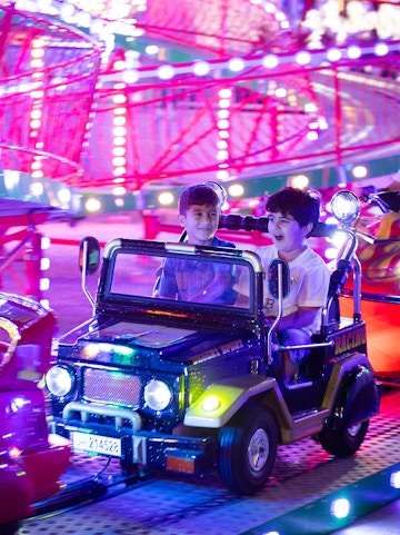 Children enjoying a ride at Lusail Winter Wonderland with colorful lights in the background.