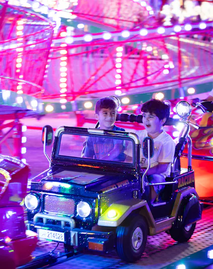 Children enjoying a ride at Lusail Winter Wonderland with colorful lights in the background.