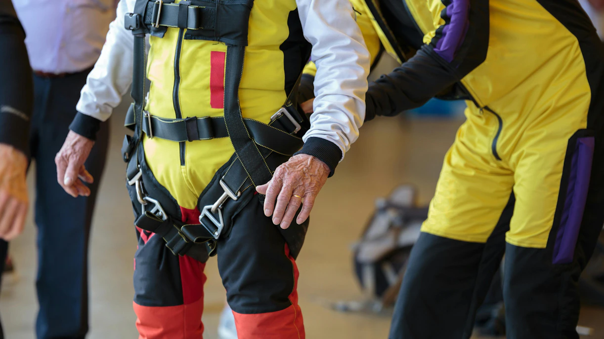 Skydiving instructor assists apprentice with parachute harness adjustment.
