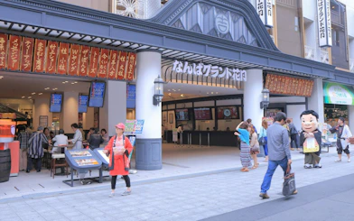 Entrance to Namba Grand Kagetsu theater in Osaka with people exploring nearby food stalls.