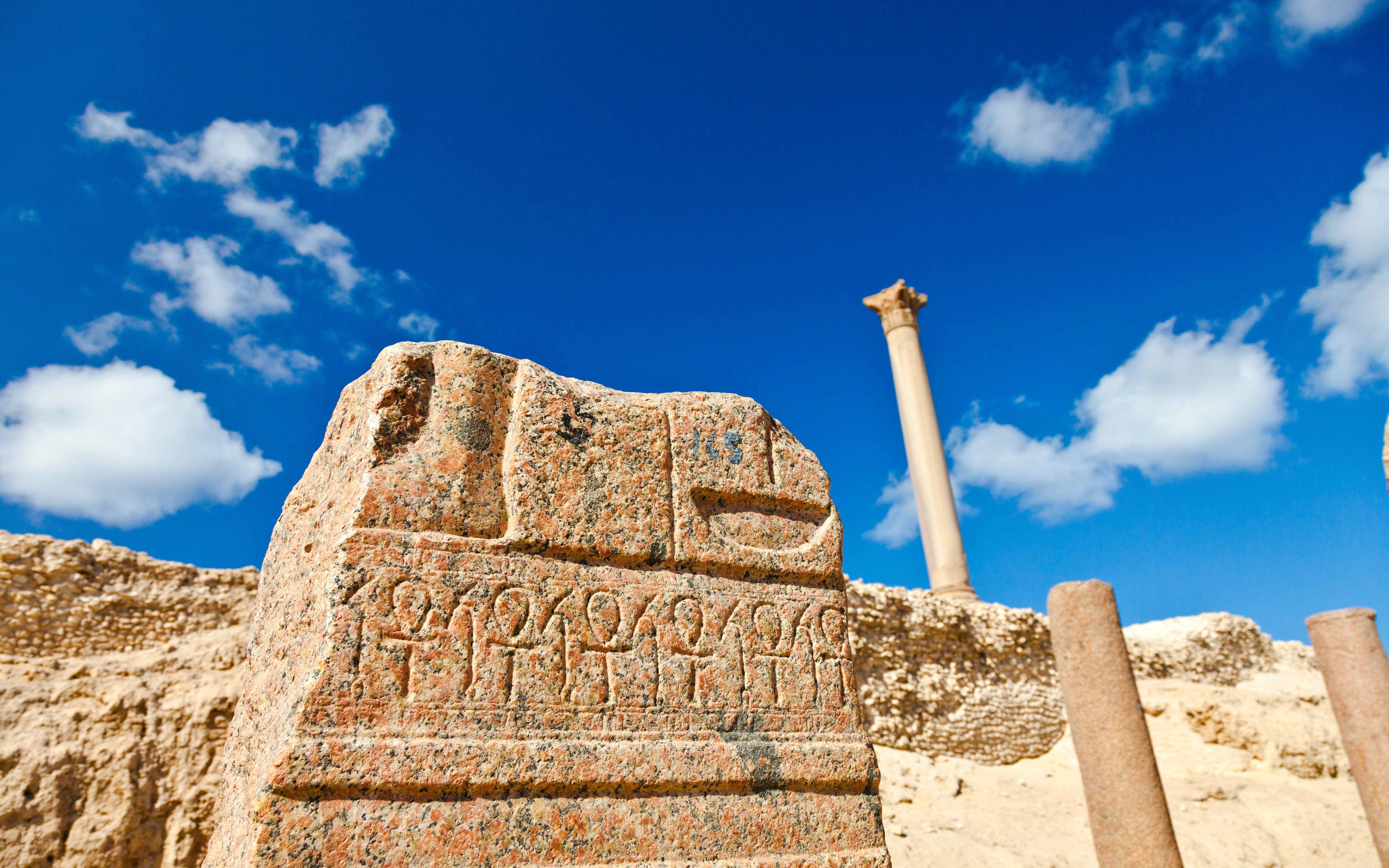Ancient carvings near Pompey's Pillar in Alexandria, Egypt, with clear blue sky.