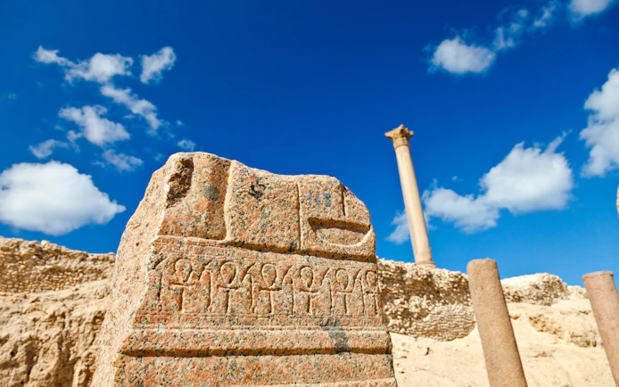 Ancient carvings near Pompey's Pillar in Alexandria, Egypt, with clear blue sky.