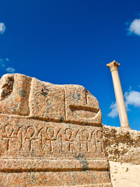 Ancient carvings near Pompey's Pillar in Alexandria, Egypt, with clear blue sky.