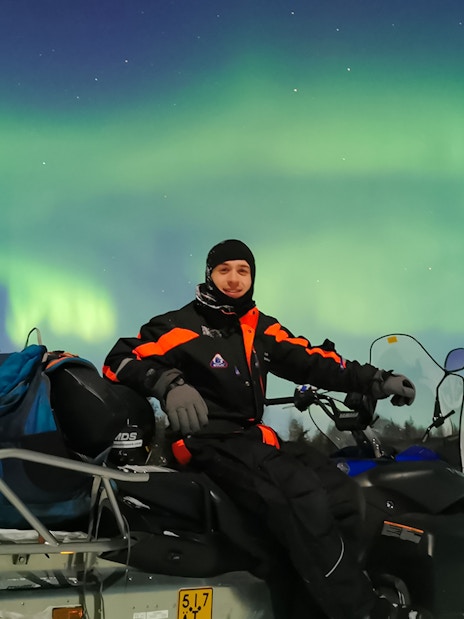 Man on snowmobile under Northern Lights in Levi, Finland.