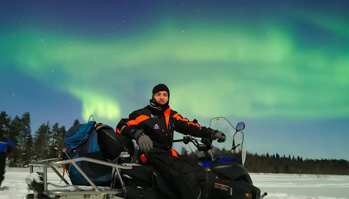 Man on snowmobile under Northern Lights in Levi, Finland.