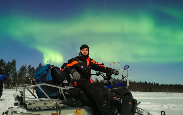 Man on snowmobile under Northern Lights in Levi, Finland.