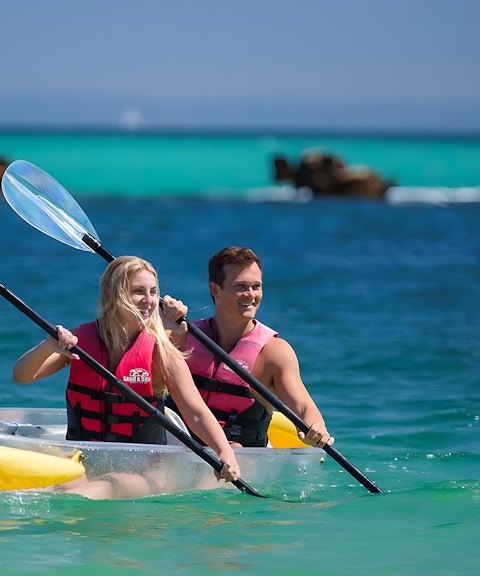 Couple kayaking in transparent kayak on clear waters of Moreton Island, Australia.