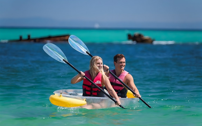 Couple kayaking in transparent kayak on clear waters of Moreton Island, Australia.