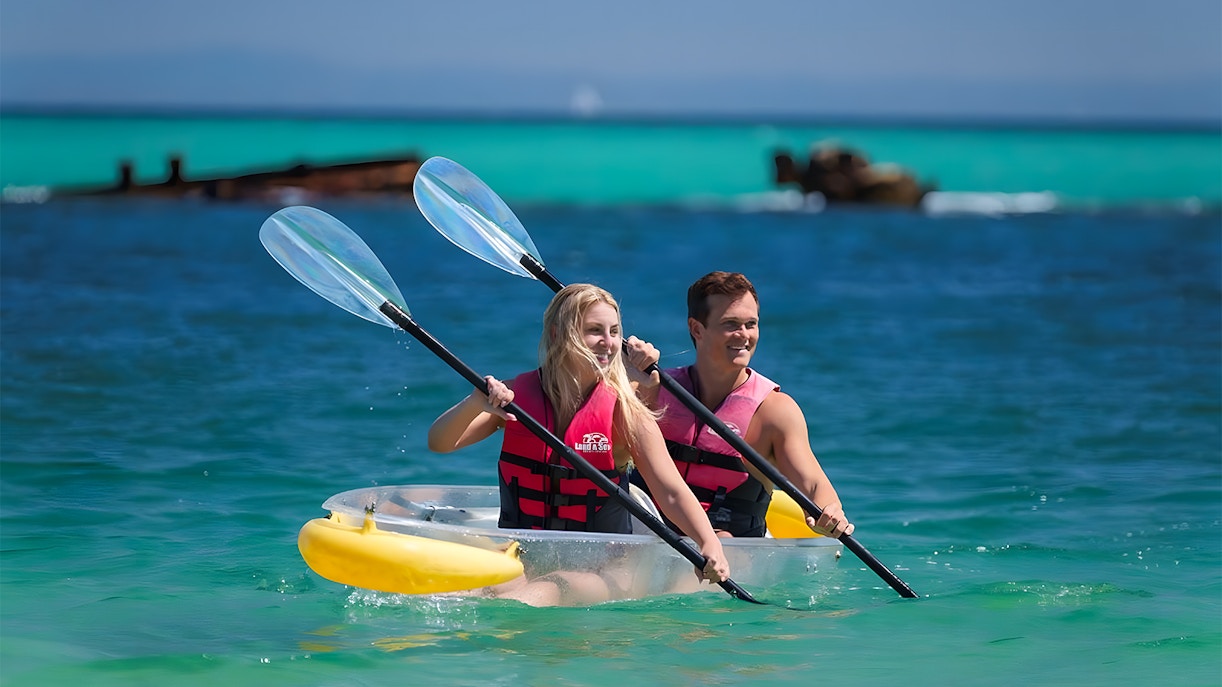Couple kayaking in transparent kayak on clear waters of Moreton Island, Australia.