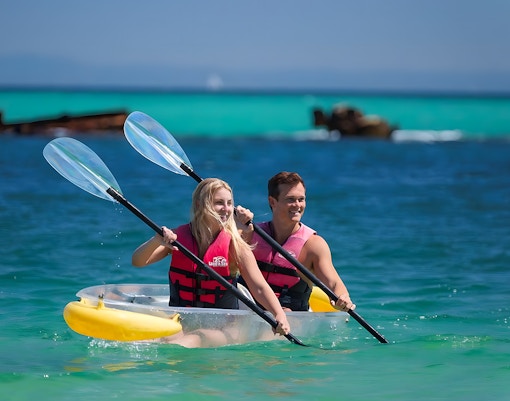 Couple kayaking in transparent kayak on clear waters of Moreton Island, Australia.